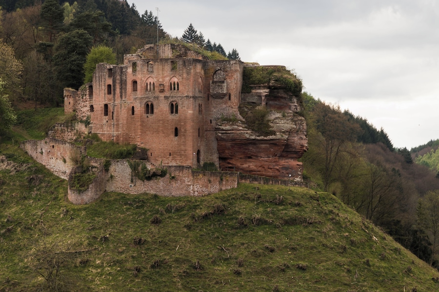 A historic stone castle on a grassy hill with a rocky cliff.