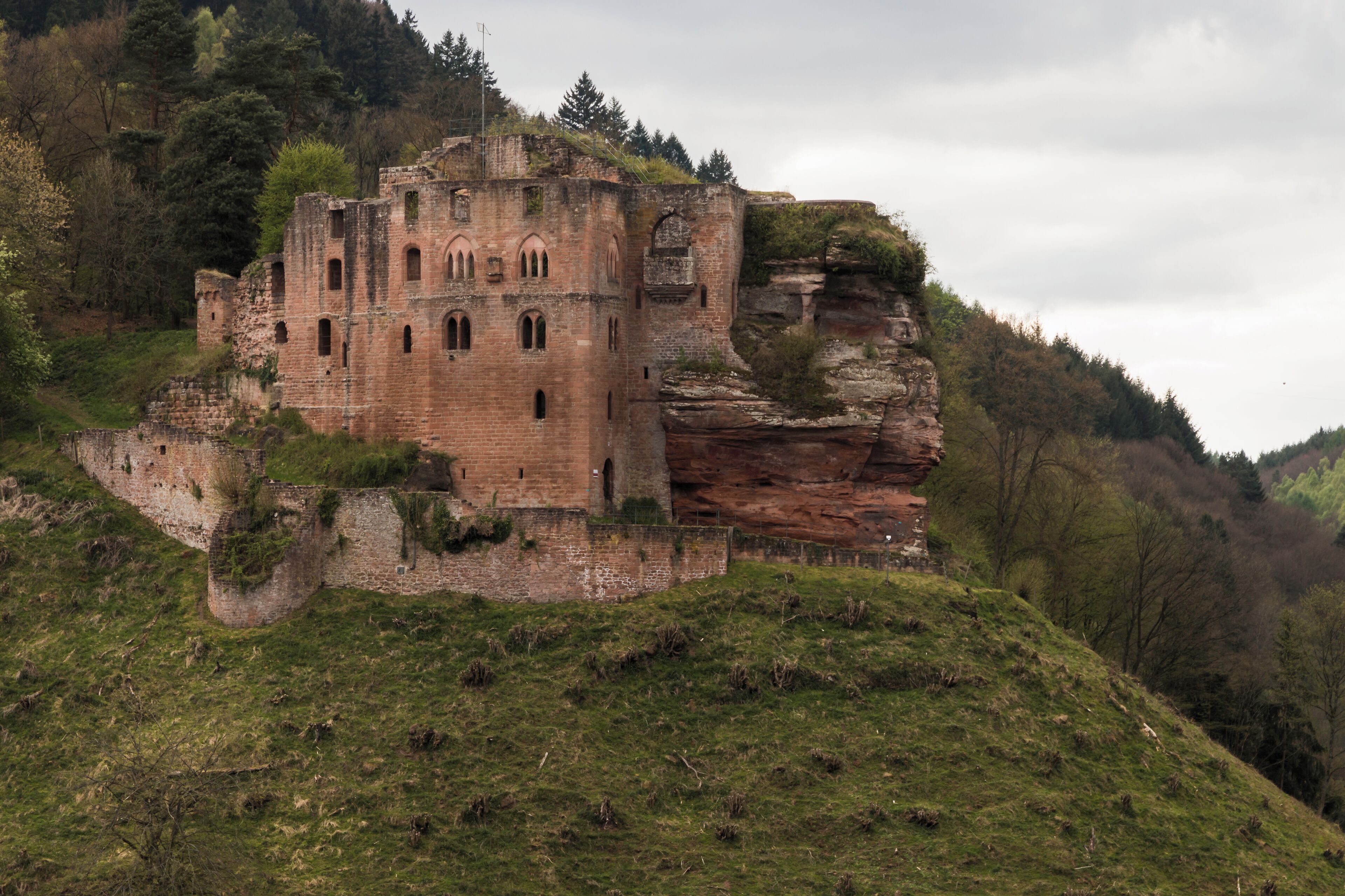 A historic stone castle on a grassy hill with a rocky cliff.
