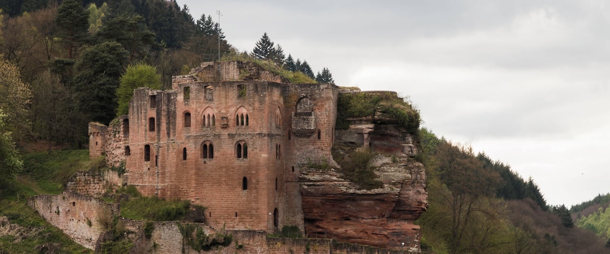 A historic stone castle on a grassy hill with a rocky cliff.