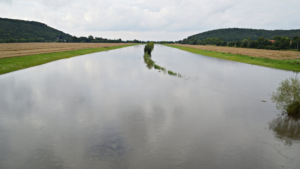 Ein breiter Fluss mit einer schmalen Landzunge in der Mitte, umgeben von Feldern und Hügeln.
