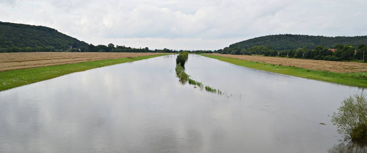 A wide river with a narrow strip of land in the middle, surrounded by fields and hills.