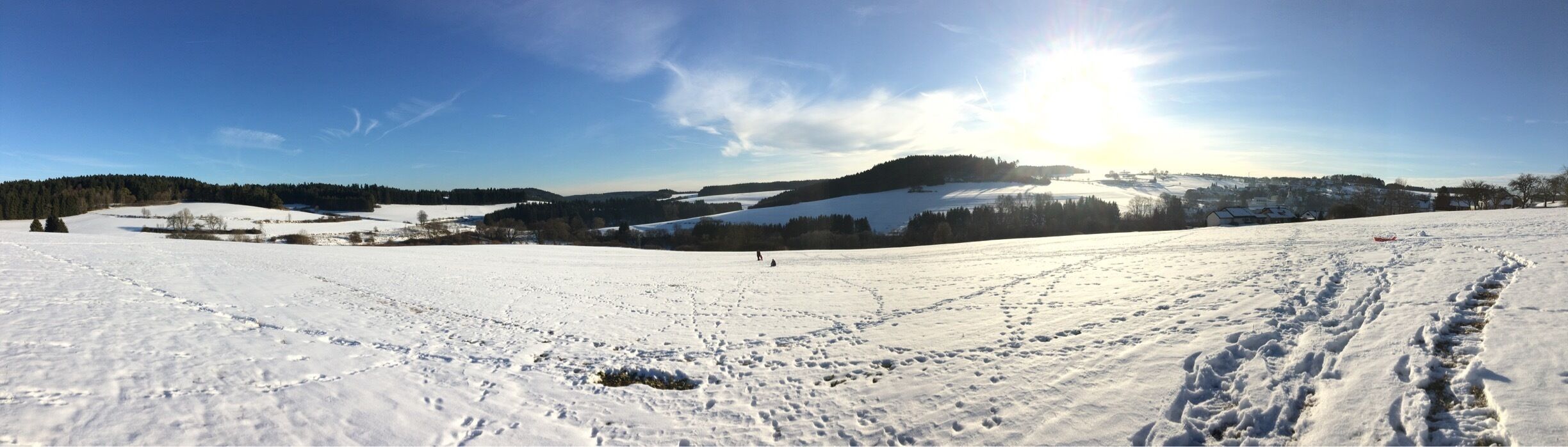 A snowy landscape with footprints, a hill, and a village in the background.