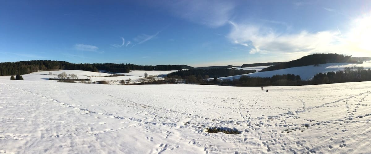 A snowy landscape with footprints, a hill, and a village in the background.