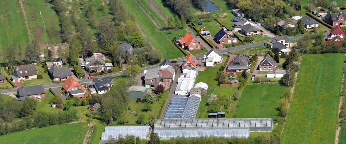 An aerial view of a rural area with houses, green fields, and a large greenhouse.