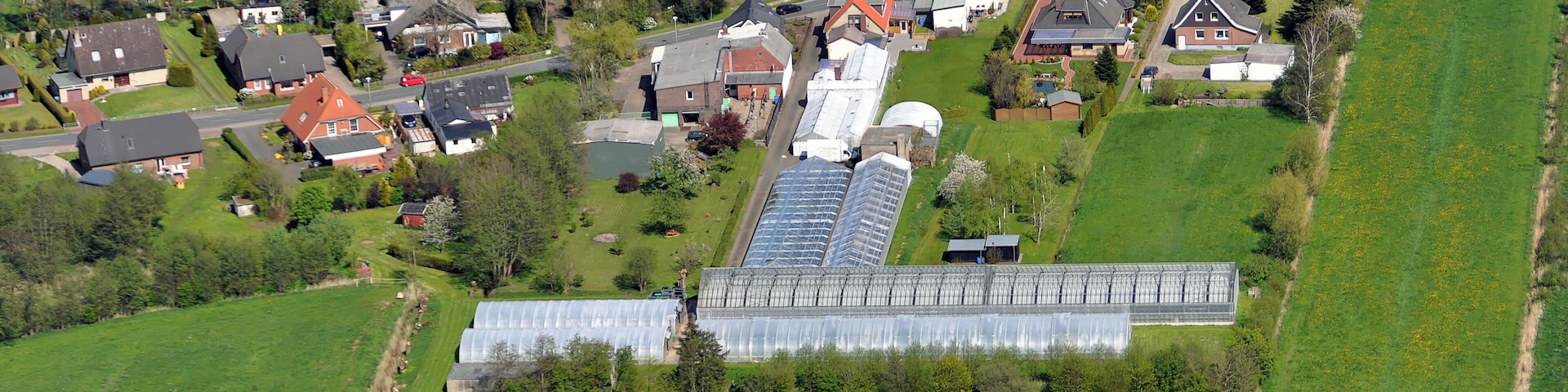 An aerial view of a rural area with houses, green fields, and a large greenhouse.