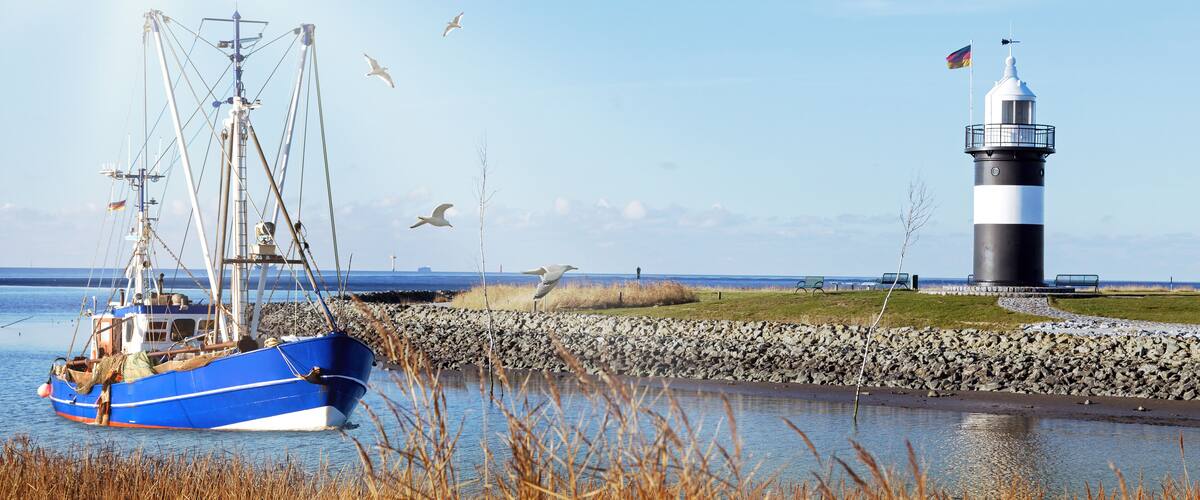 A blue fishing boat docked near a lighthouse and rocky shore.