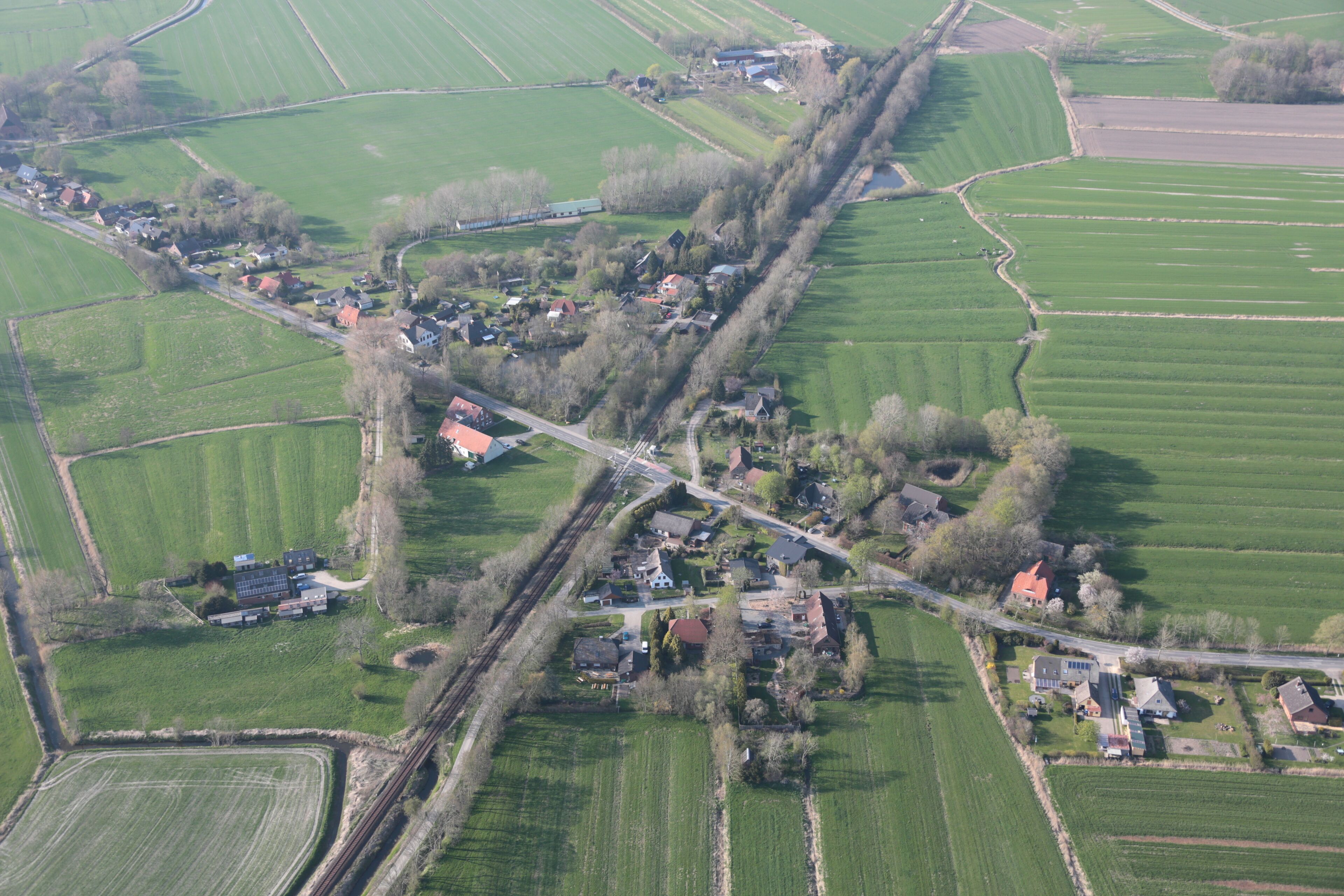 An aerial view of a rural area with fields, a railway line, and scattered houses.