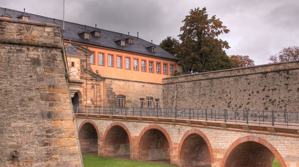 Un bâtiment historique en pierre, doté d’un toit rouge, d’un mur en pierre et d’une série d’arcades.