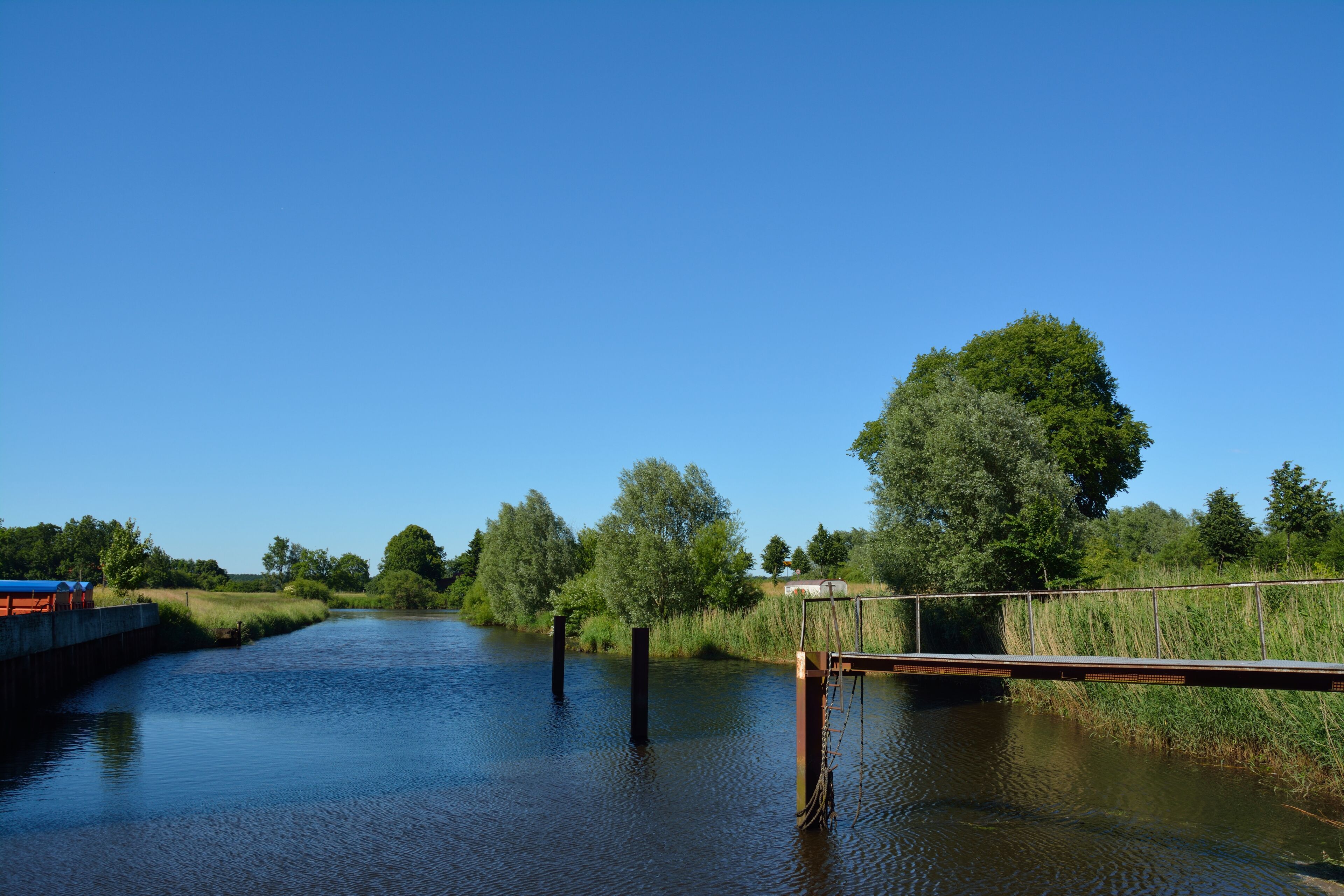 A calm river with a wooden bridge, surrounded by lush greenery and trees.