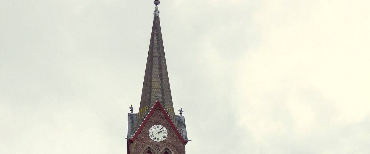A church with a tall steeple, a clock, and a cross at the top.