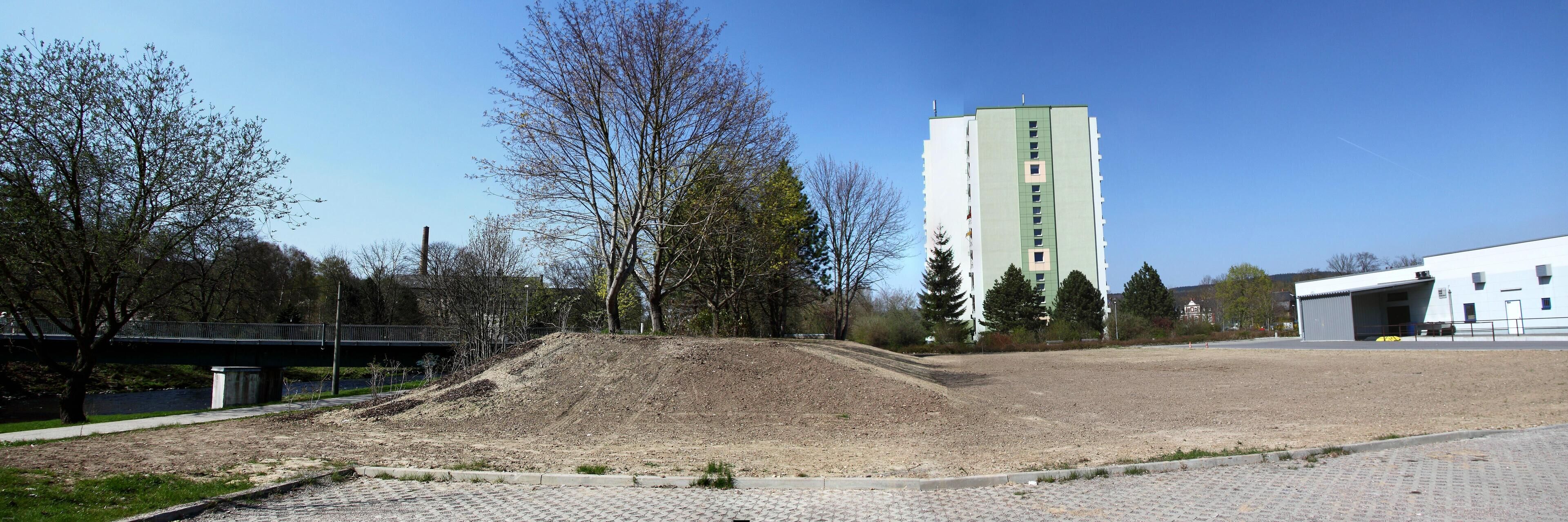 A construction site with a large pile of dirt, a bridge, and a tall building in the background.