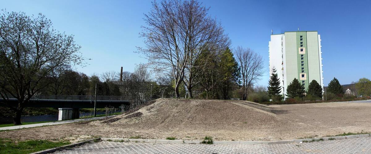 A construction site with a large pile of dirt, a bridge, and a tall building in the background.