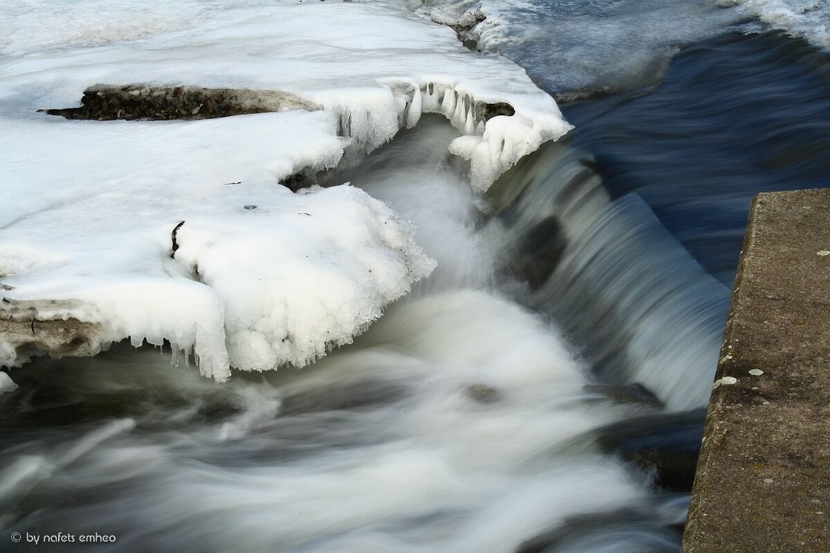 A frozen waterfall with ice formations and a concrete edge.