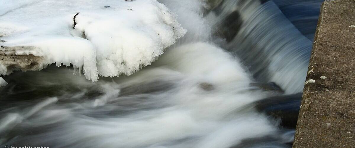 A frozen waterfall with ice formations and a concrete edge.
