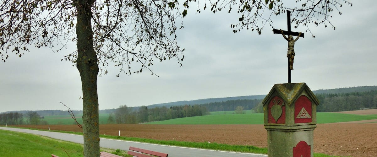 A rural landscape with a cross monument, picnic tables, and a road.