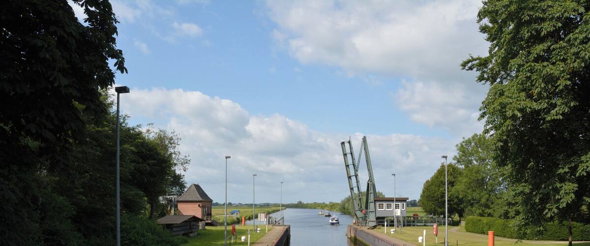 A canal with a lock mechanism, surrounded by greenery and a clear sky.