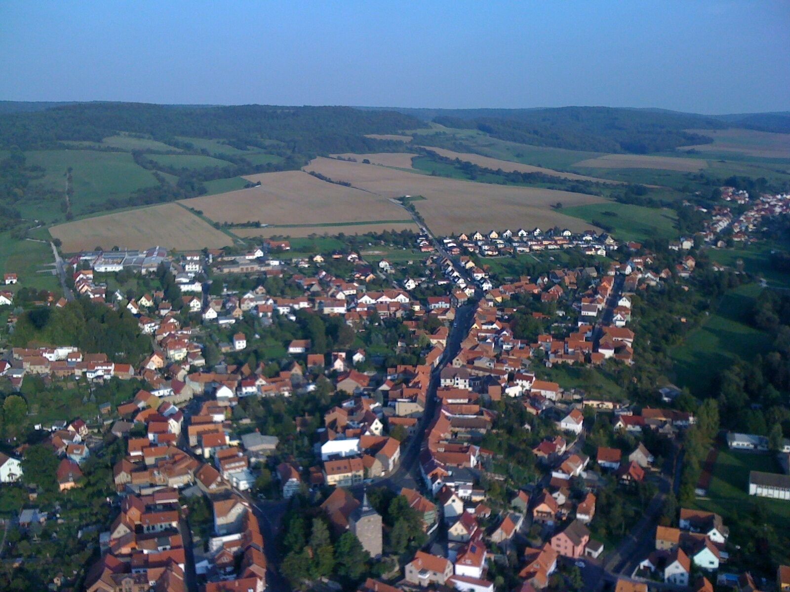 A rural village with red-roofed houses, surrounded by fields and rolling hills.