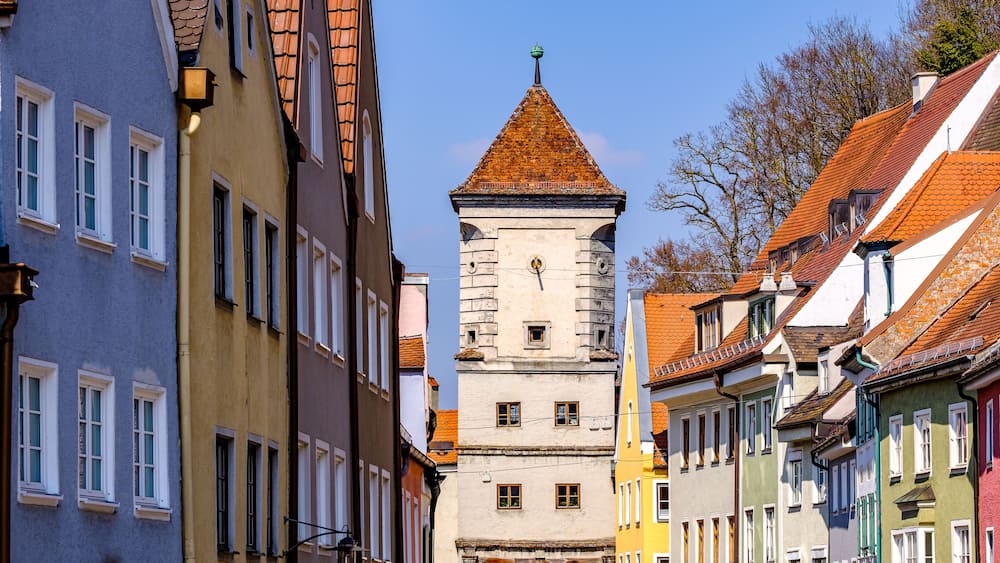 Ein historischer Turm mit einer spitzen Turmkuppel inmitten farbenfroher Gebäude.