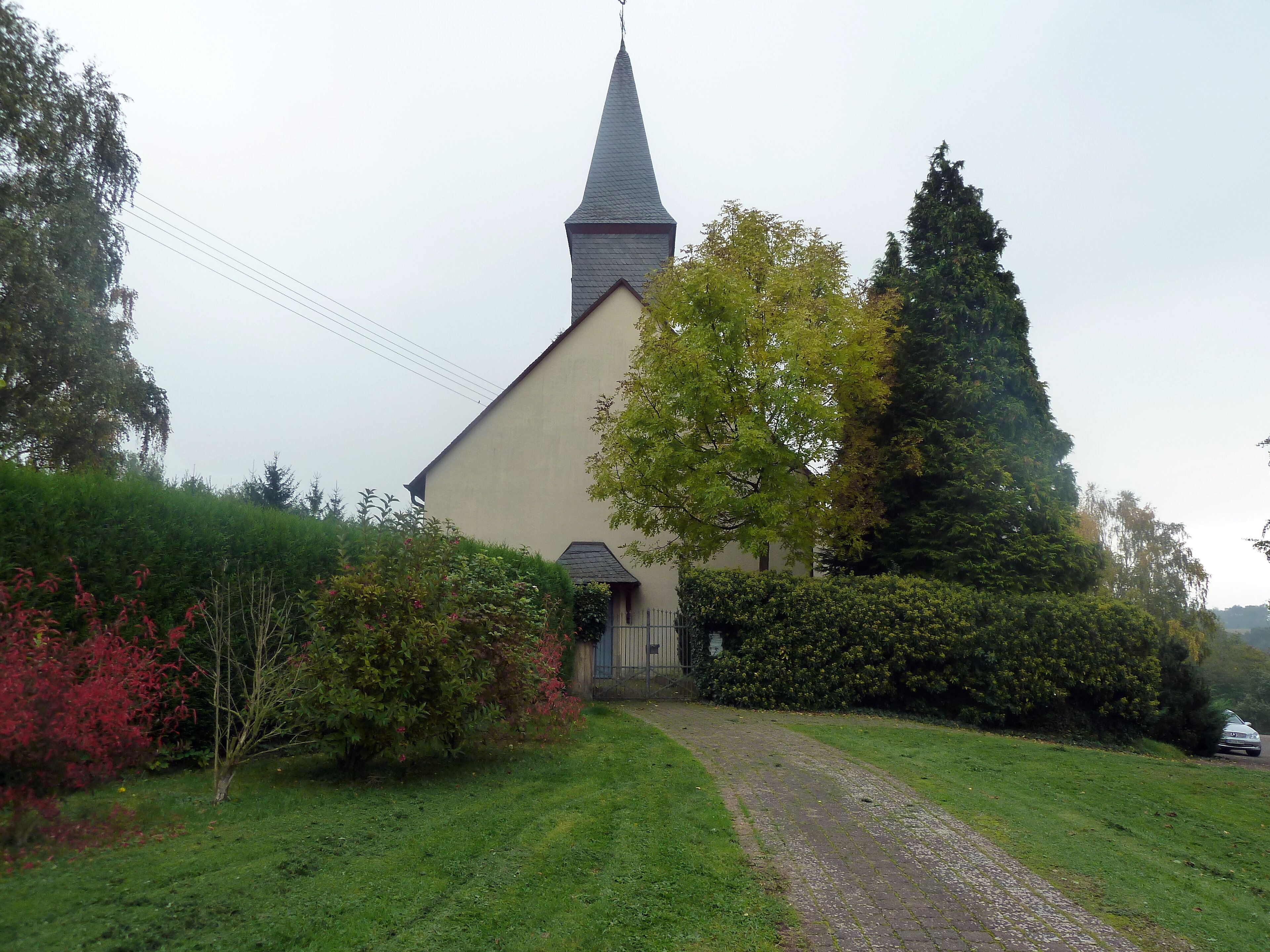 A church with a tall steeple, surrounded by lush greenery and a gravel path leading to the entrance.