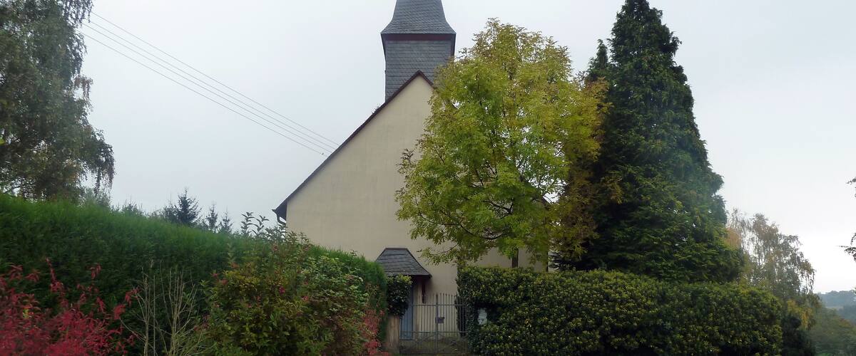 A church with a tall steeple, surrounded by lush greenery and a gravel path leading to the entrance.