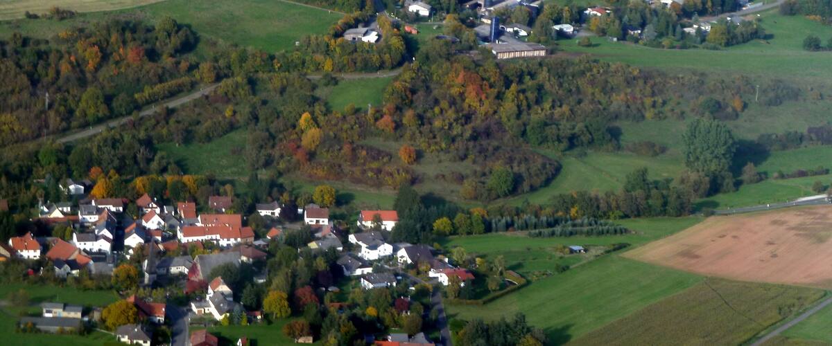 A rural landscape with rolling hills, fields, and a small village with houses and a large industrial building.