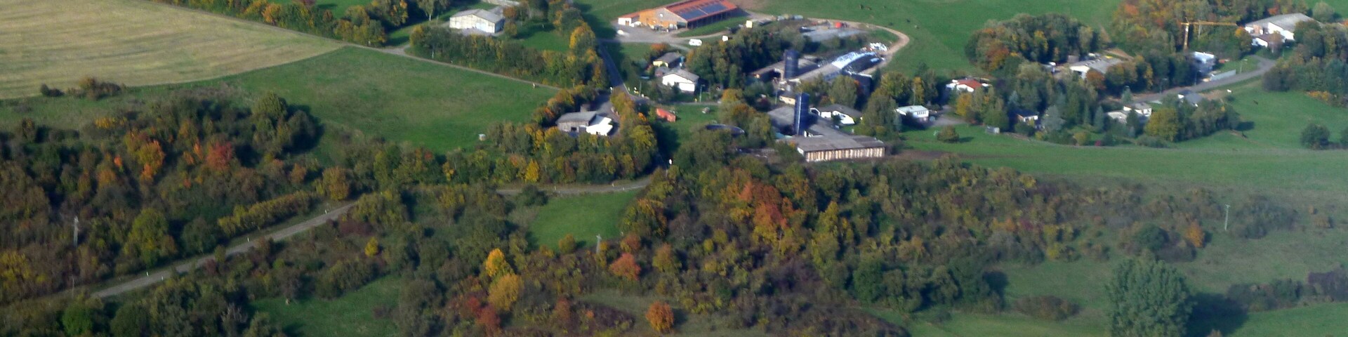 A rural landscape with rolling hills, fields, and a small village with houses and a large industrial building.