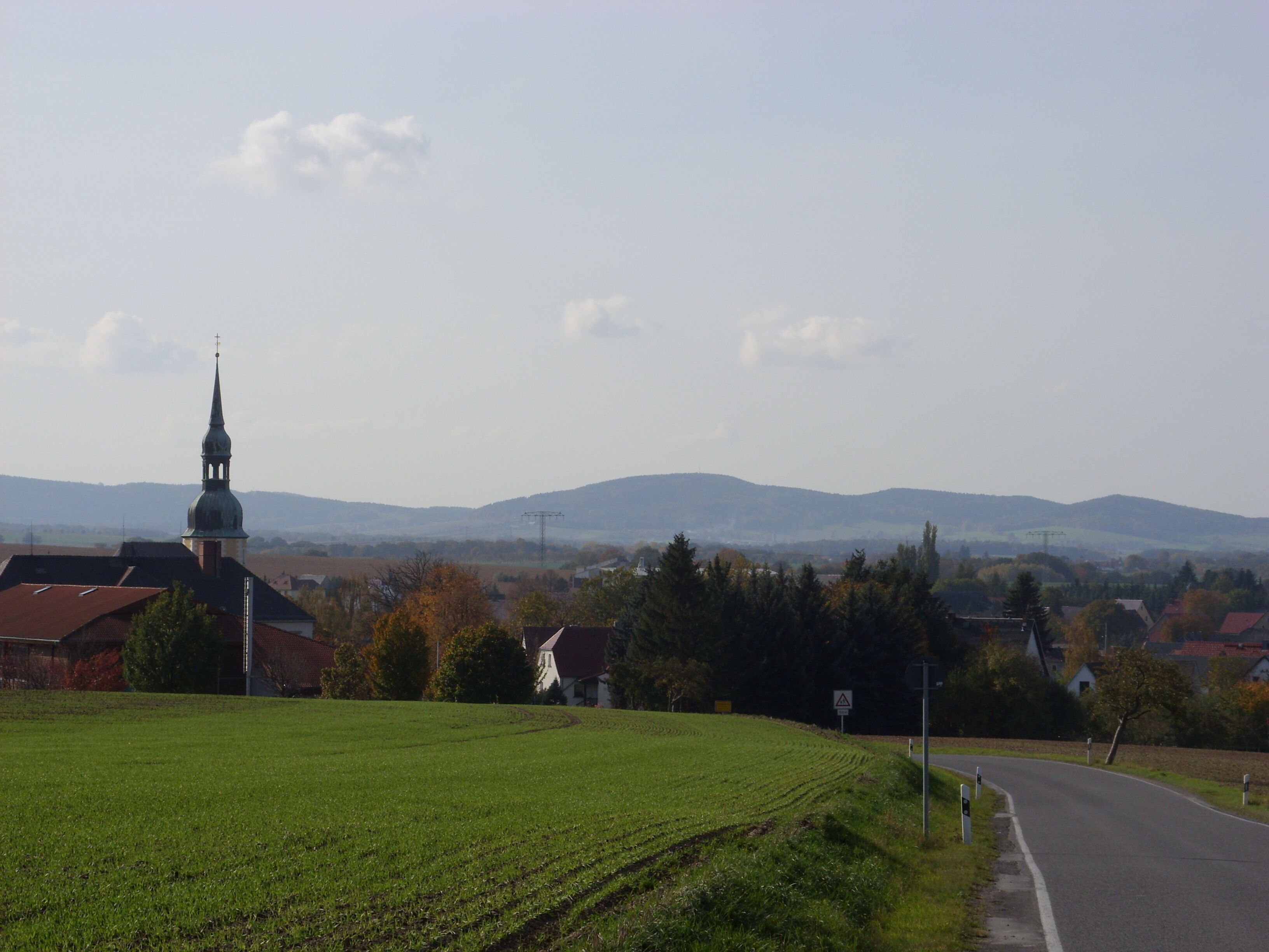 A rural landscape with a church, green fields, and distant mountains.
