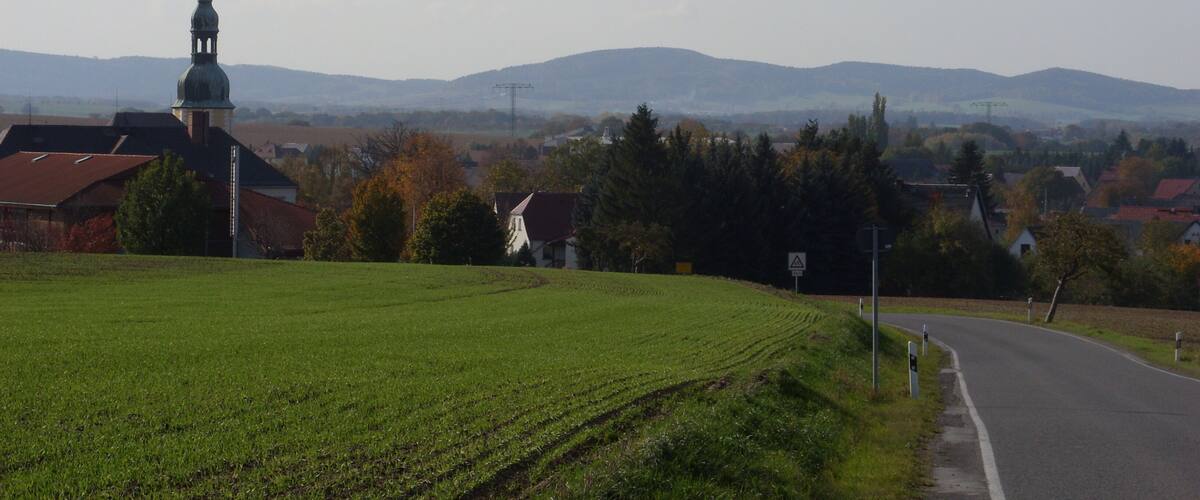 A rural landscape with a church, green fields, and distant mountains.