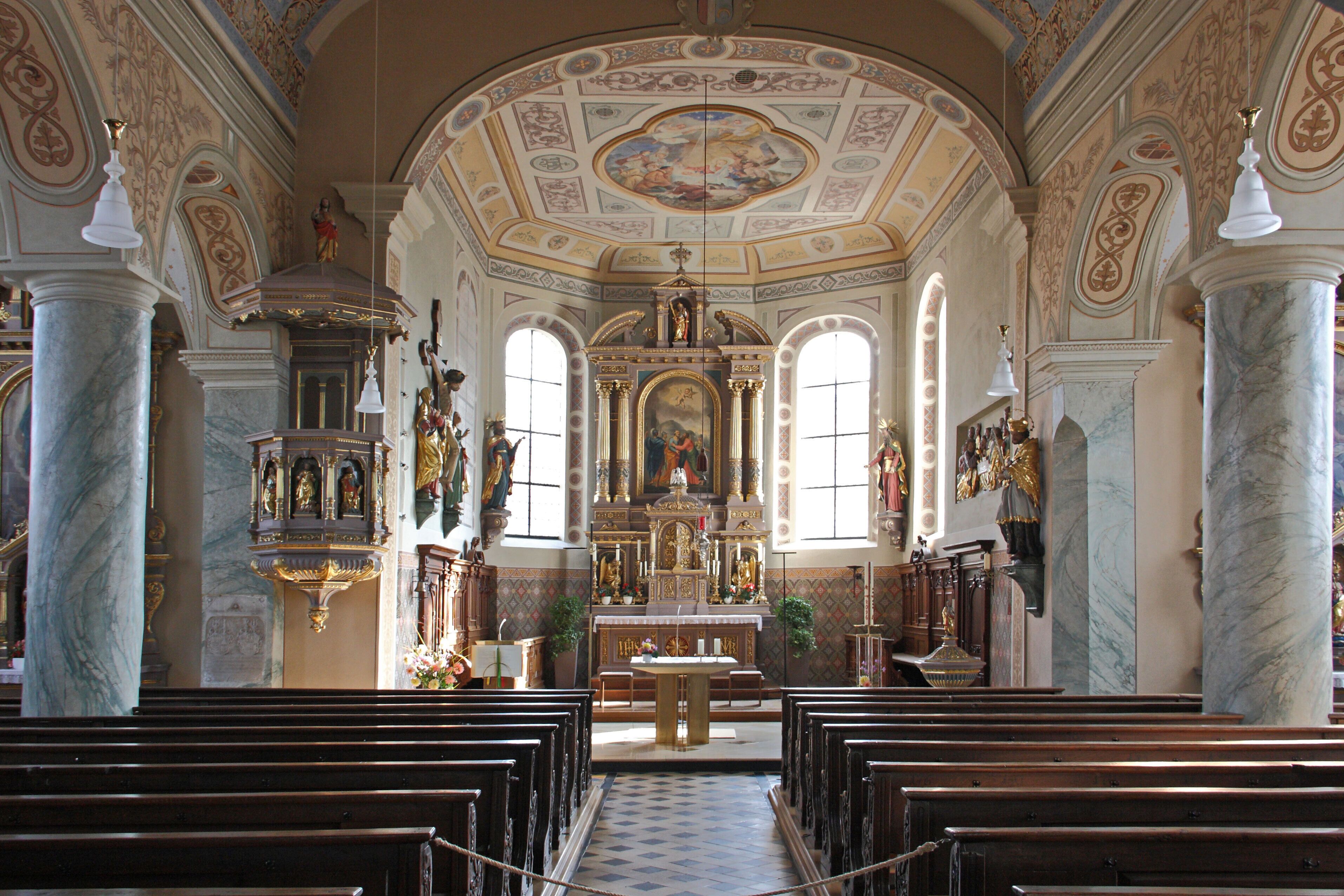 An ornate church interior with marble columns, a central altar, and religious statues.