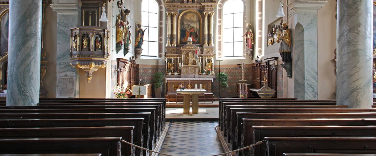 An ornate church interior with marble columns, a central altar, and religious statues.