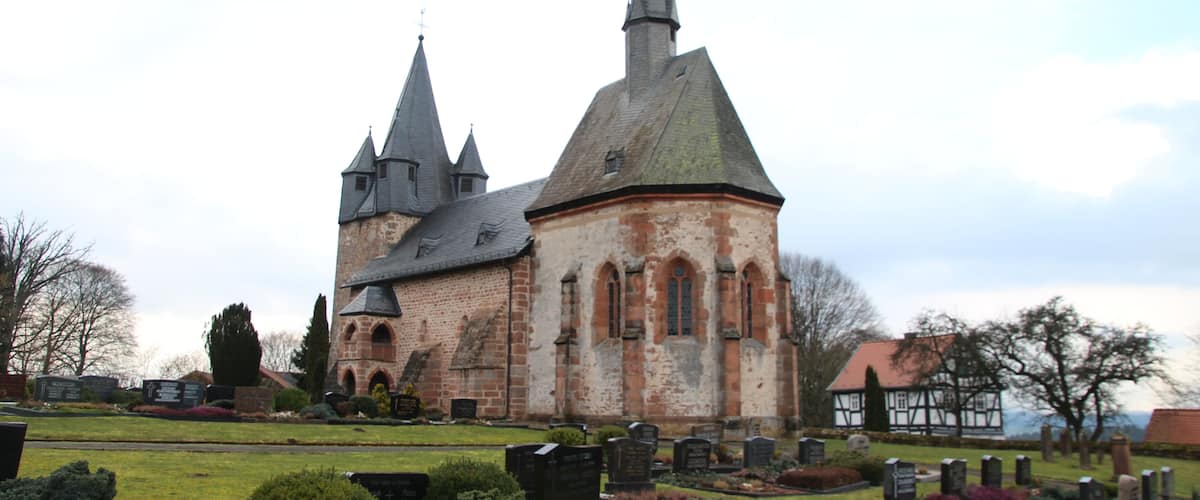 A historic church with a tall spire and multiple smaller towers, surrounded by a cemetery with headstones.