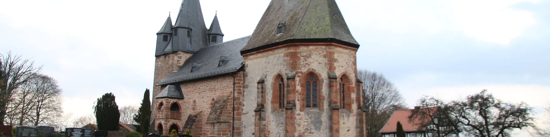 A historic church with a tall spire and multiple smaller towers, surrounded by a cemetery with headstones.