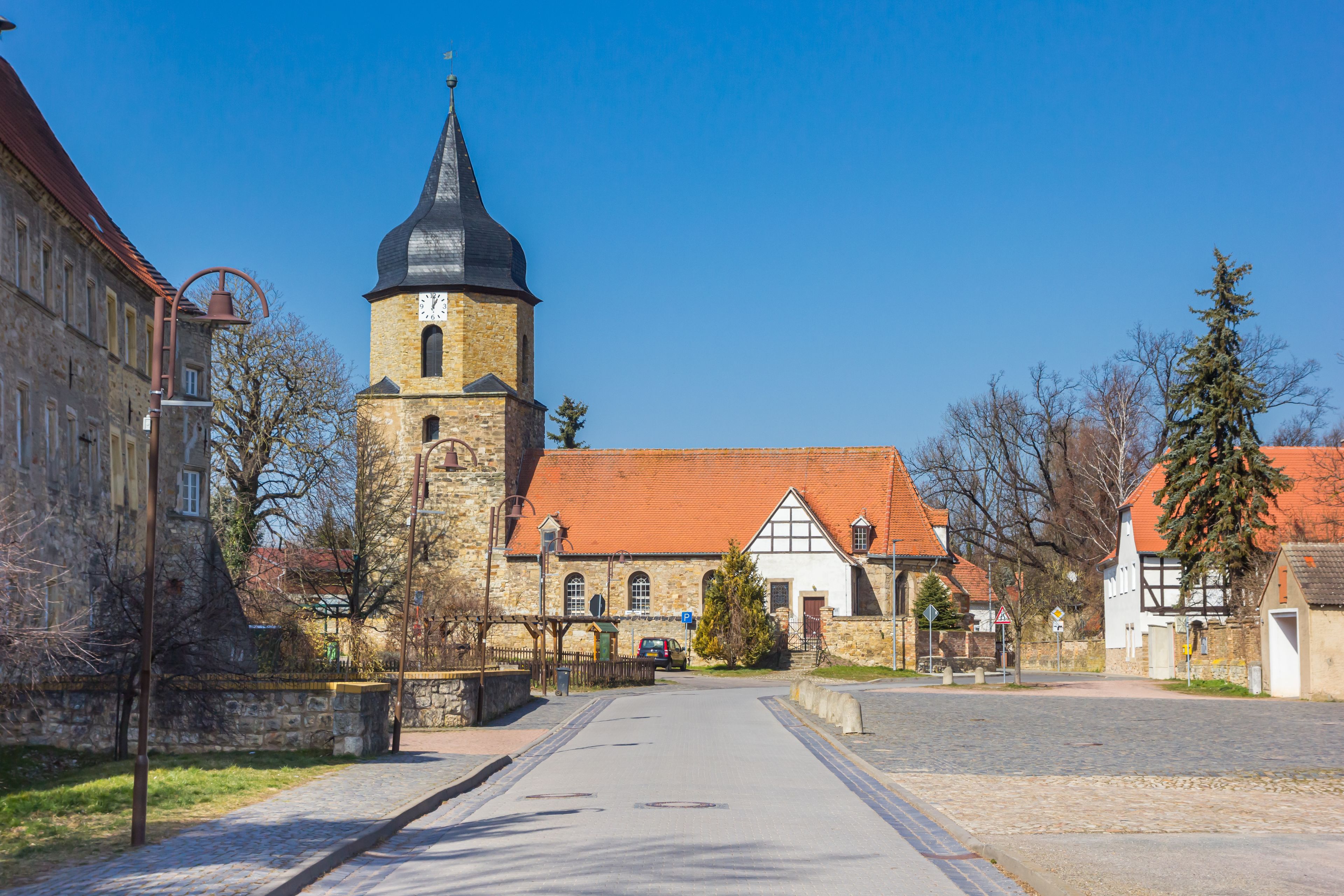 En historisk bytorv med en kirke med et markant tårn og en traditionel bygning med rødt tegltag.