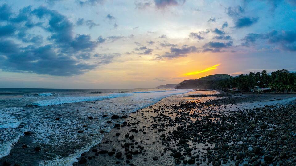 A beach with waves, pebbles, and a sunset.