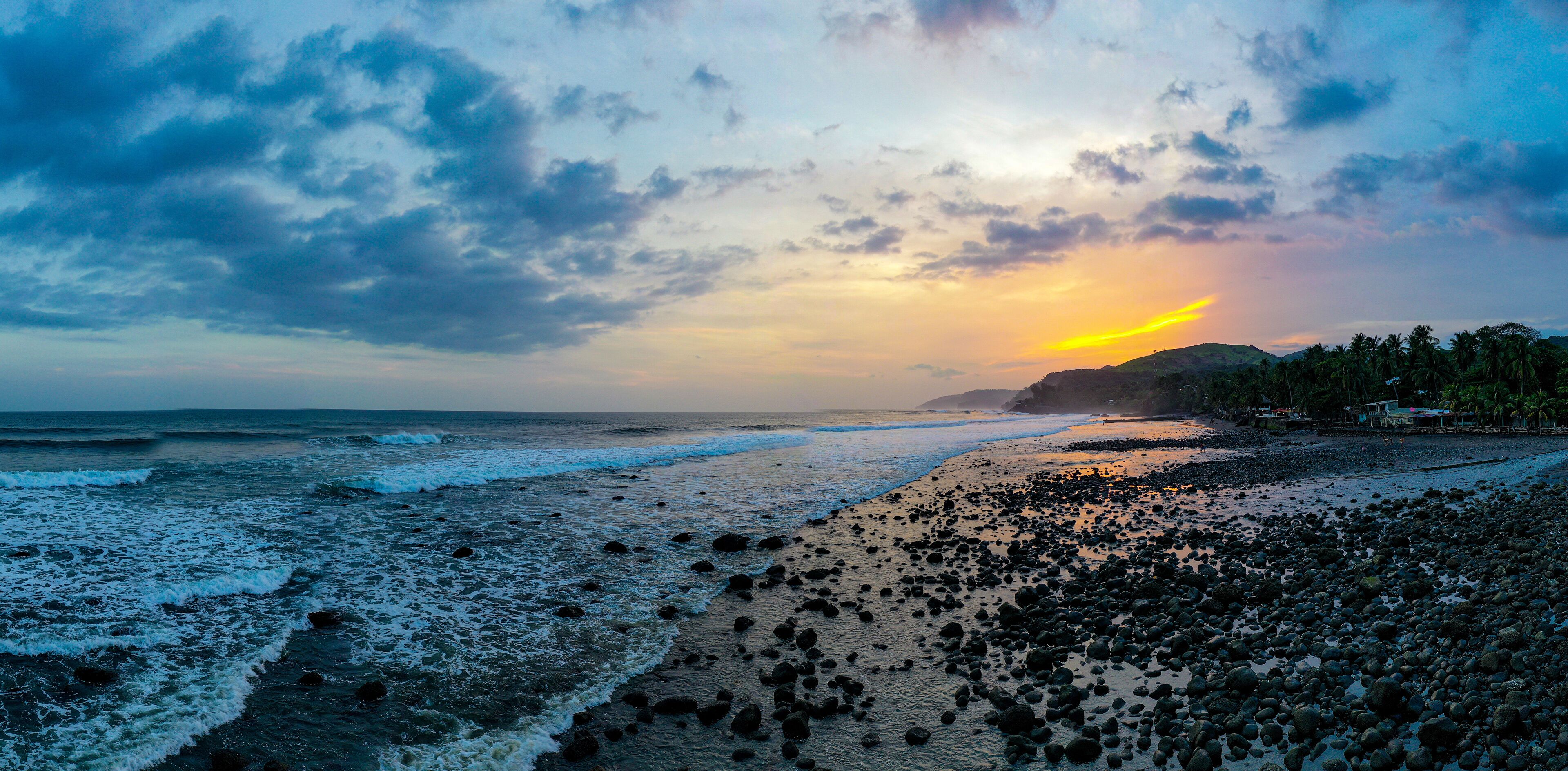 A beach with waves, pebbles, and a sunset.