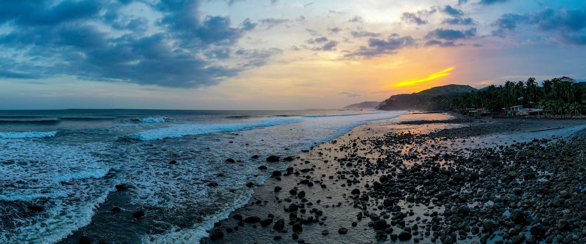 A beach with waves, pebbles, and a sunset.