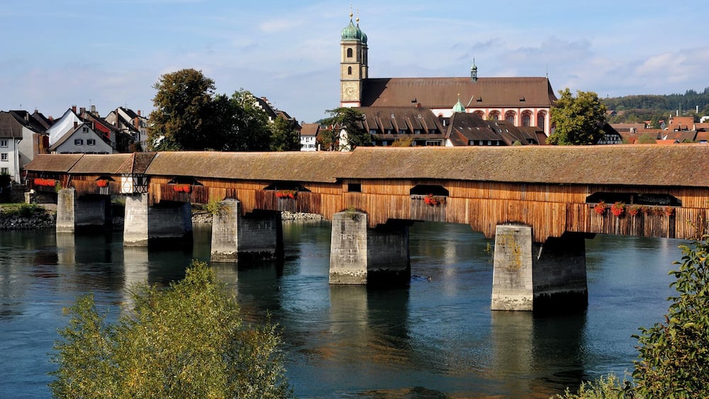 A wooden bridge over a river with a church tower in the background.