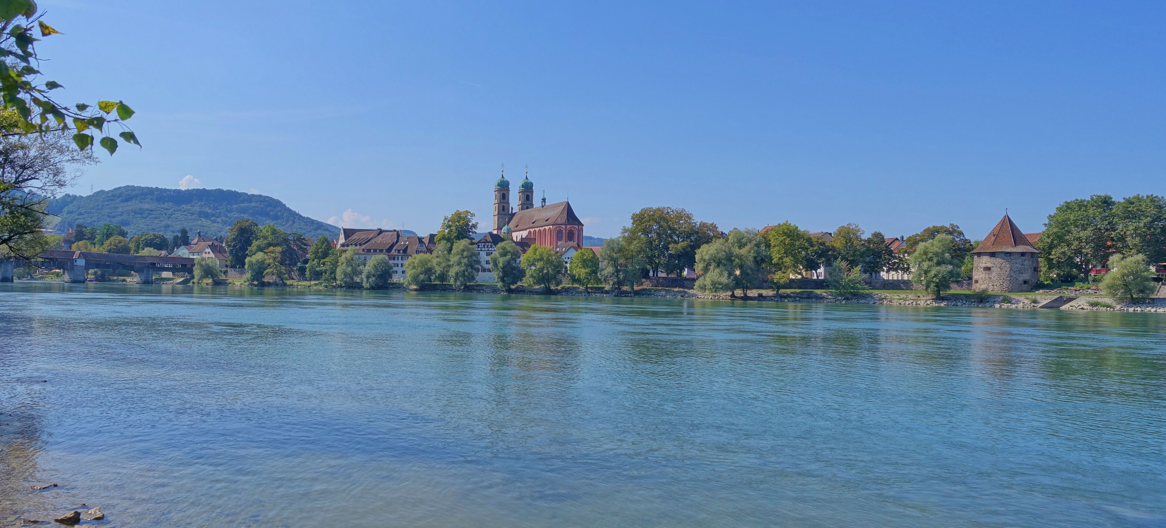 A river with a bridge, a church with two towers, and a castle-like structure.