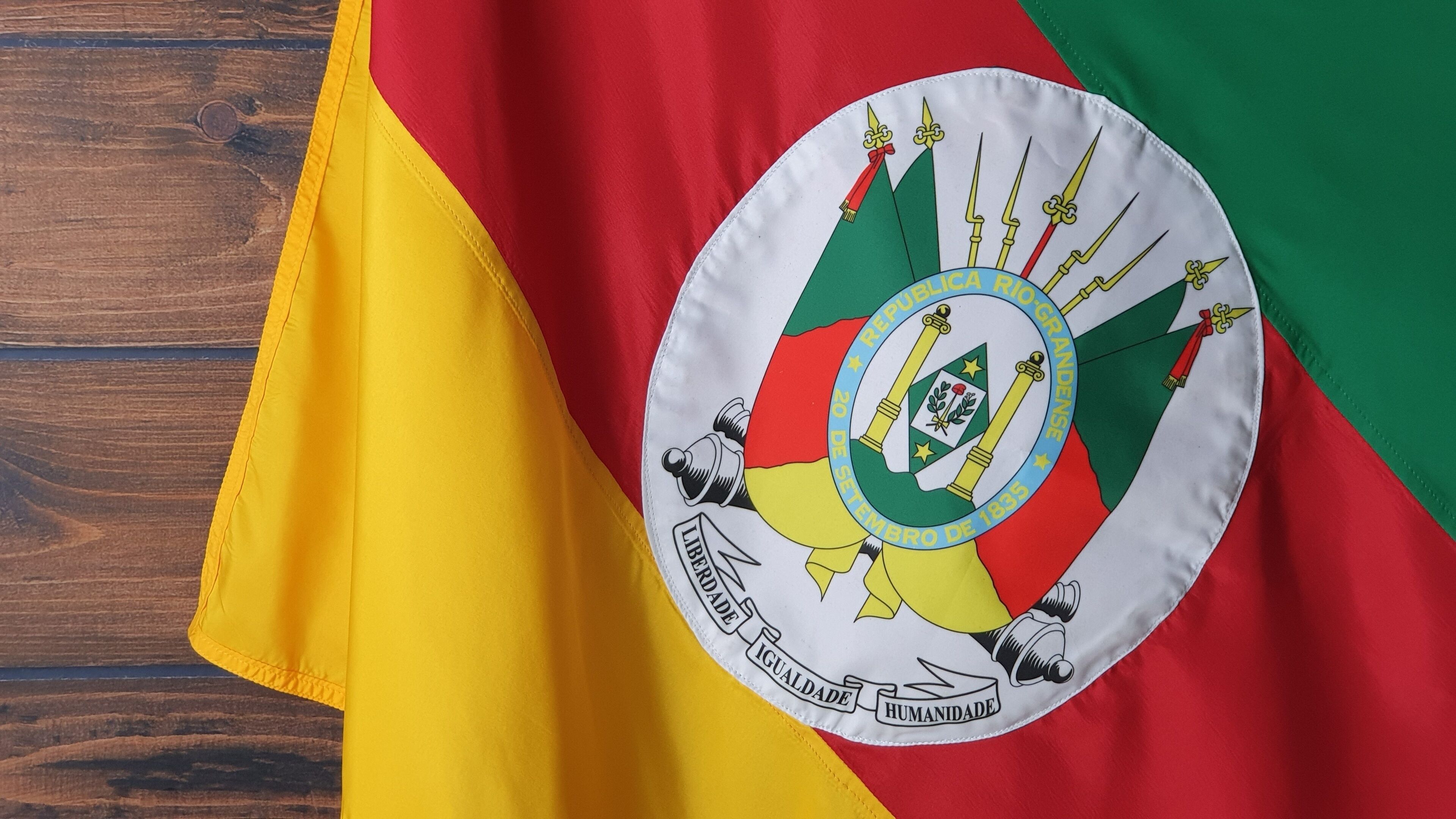 A flag with a circular emblem featuring a coat of arms, the date "20 de Setiembre de 1835," and the words "Liberdade, Igualdade, Humanidade."