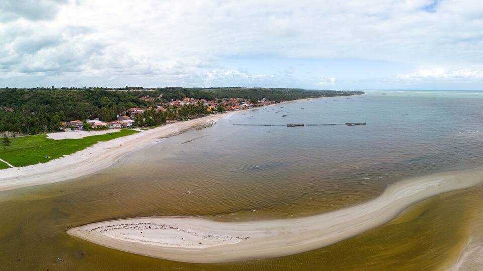 A coastal landscape with a beach, a small island, and a town in the background.