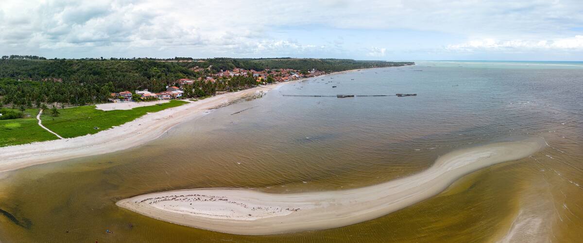 A coastal landscape with a beach, a small island, and a town in the background.