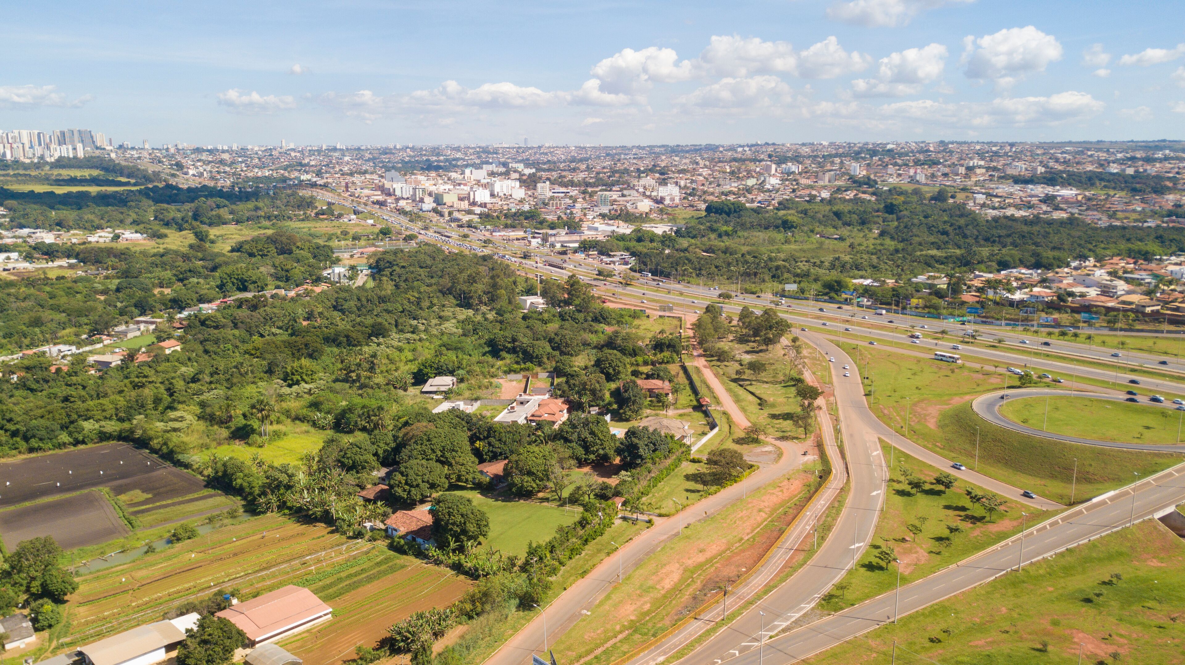 An aerial view of a city with a highway, green fields, and residential areas.