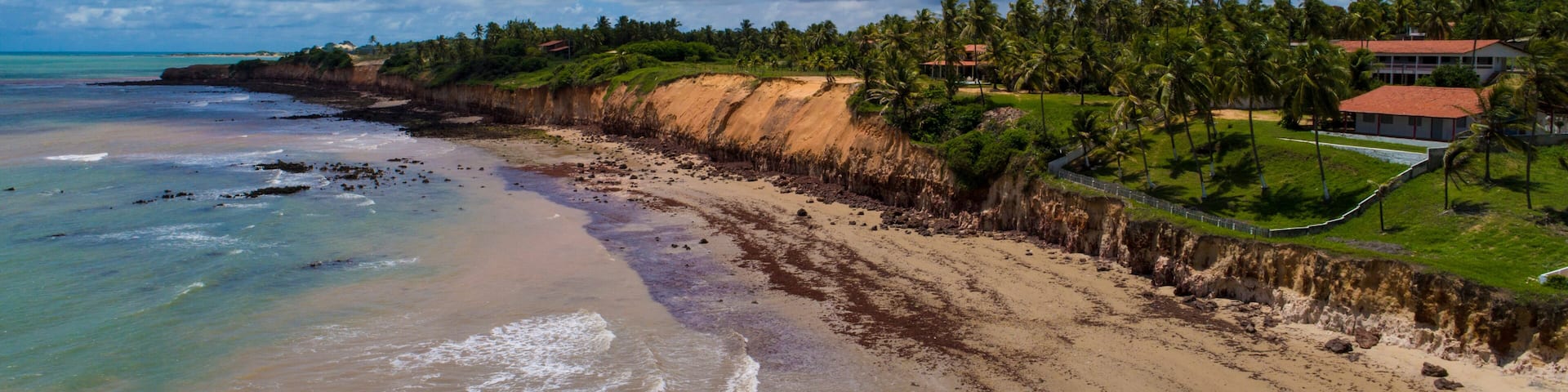 Una playa con arena, palmeras y un acantilado.