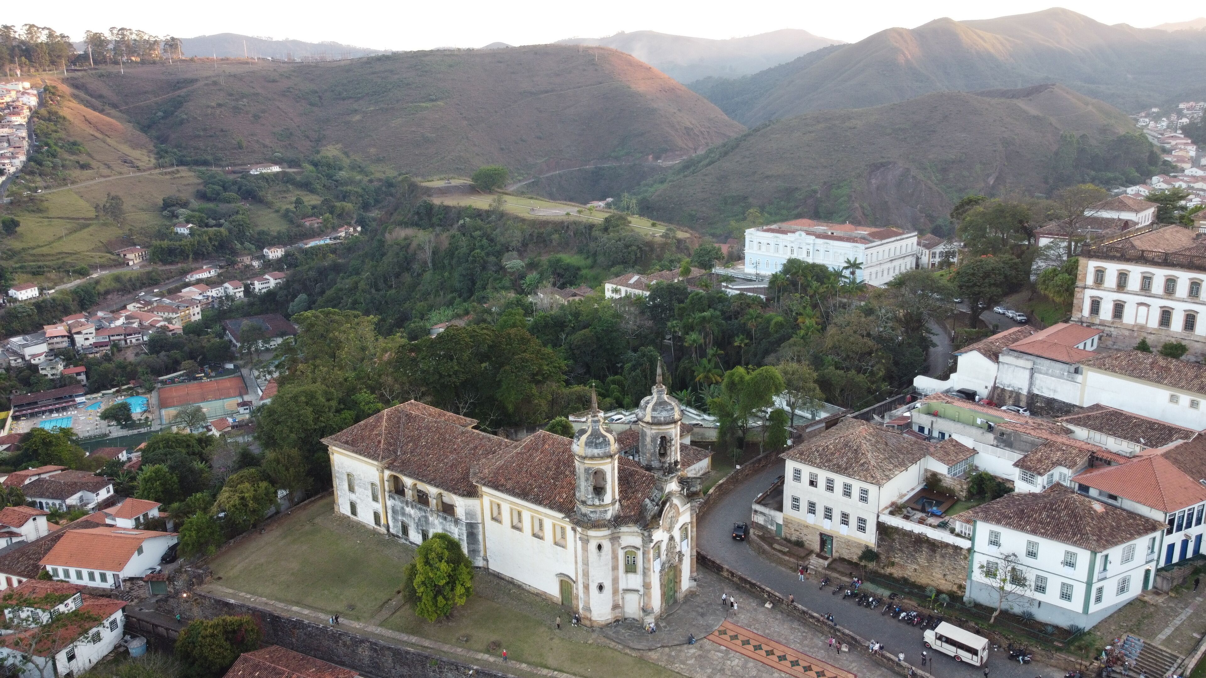 A town with a prominent church, surrounded by lush green hills and residential buildings.