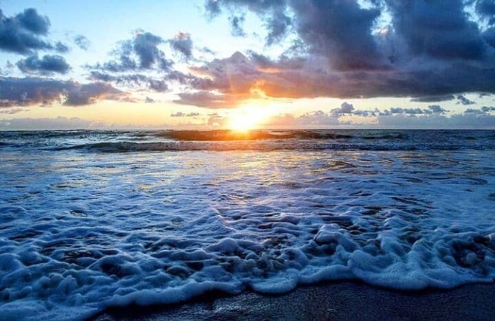 Uma praia ao pôr do sol com ondas e céu nublado.
