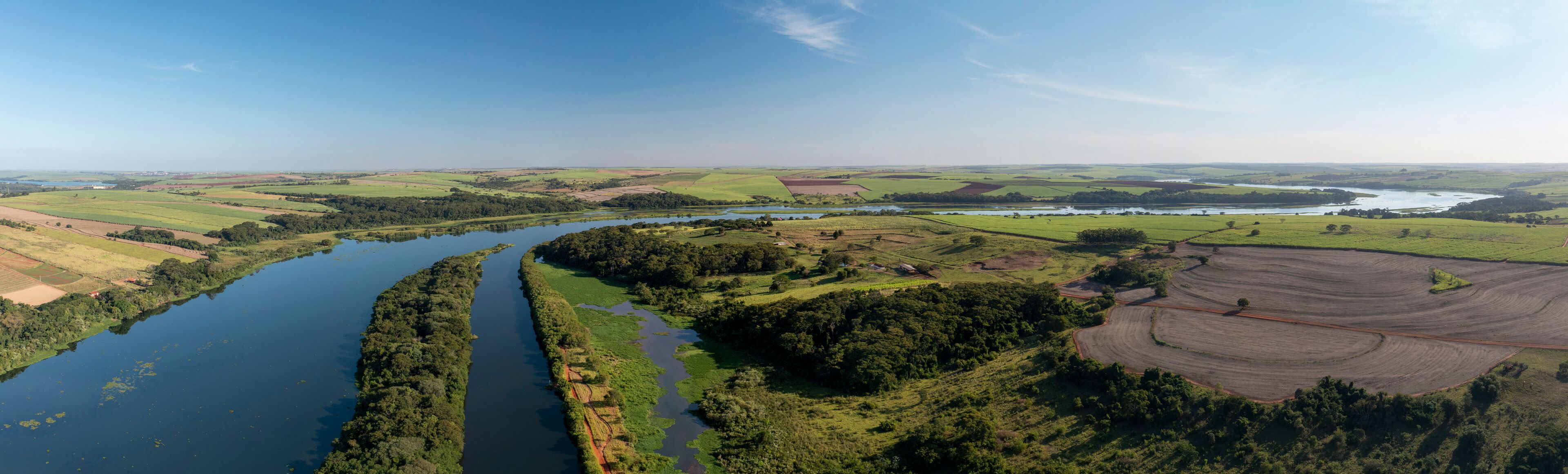 A river winding through lush green fields and forests, with a clear blue sky above.