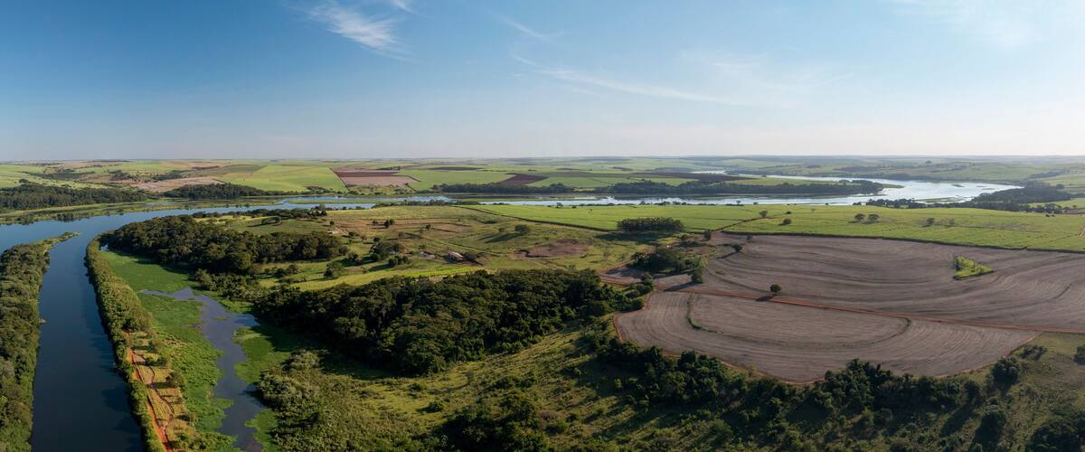 A river winding through lush green fields and forests, with a clear blue sky above.