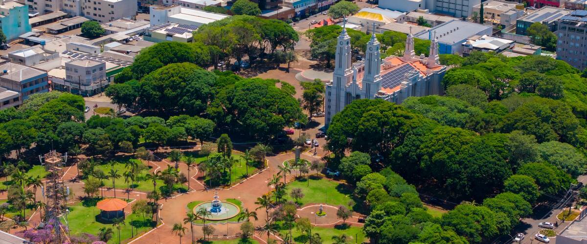 An aerial view of a city with dense greenery, a prominent church with two towers, and a mix of modern and older buildings.