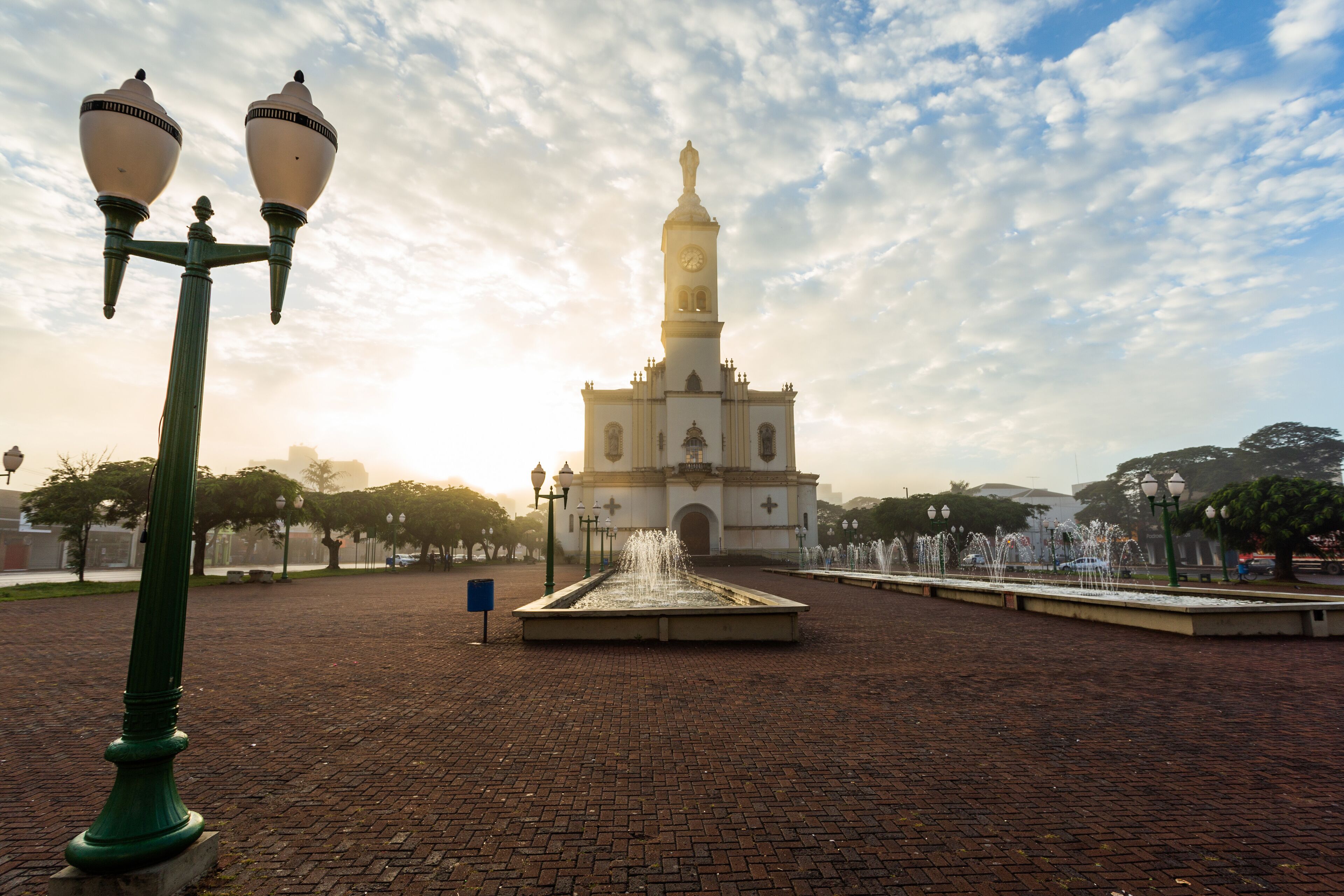 A historic building with a clock tower, a fountain, and a paved plaza.