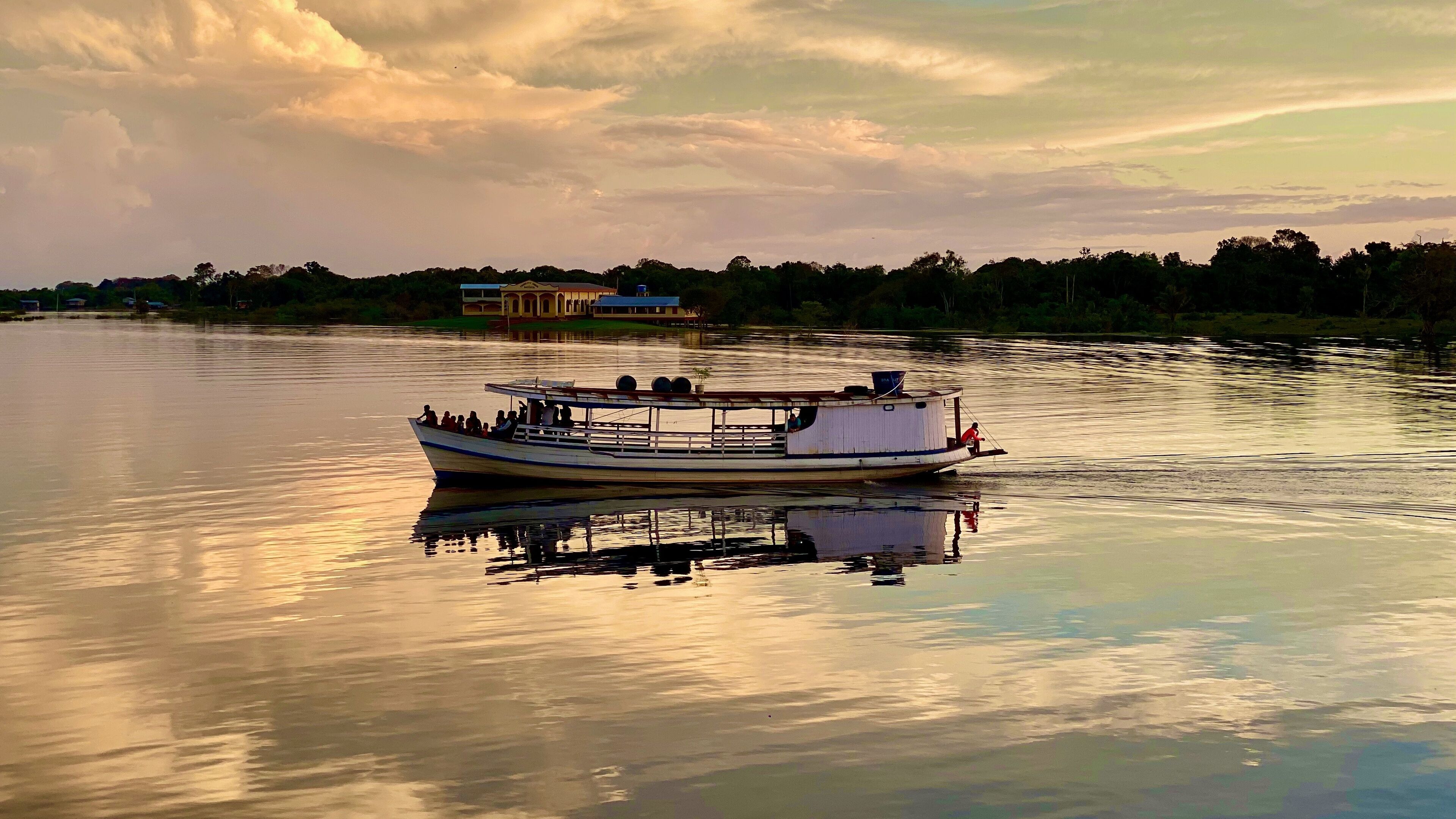 A boat on calm water with a reflection, a building in the background, and a cloudy sky.